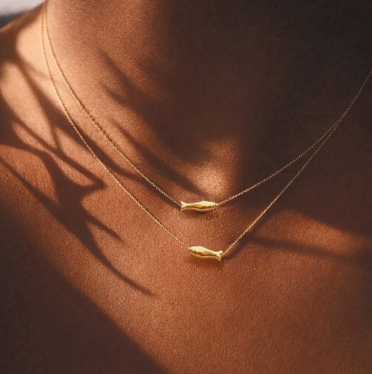 Dainty layered gold fish necklace on sun-kissed skin with artistic shadow, coastal summer jewelry by LP-Muse.