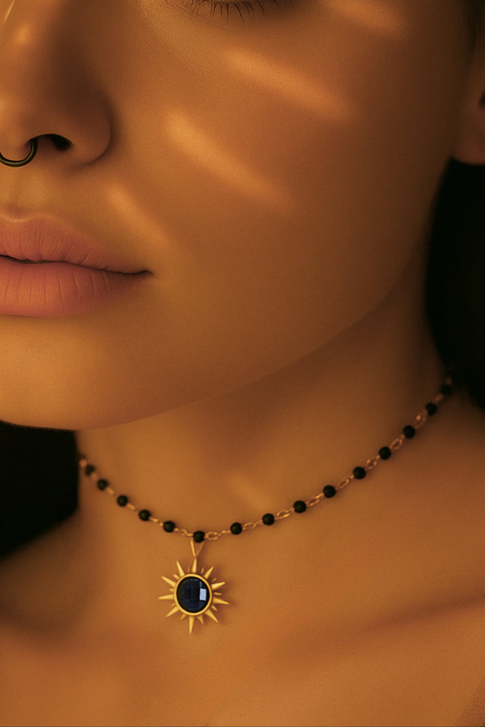 Woman wearing a sun-shaped onyx necklace with a dark stone, illuminated by sunlight