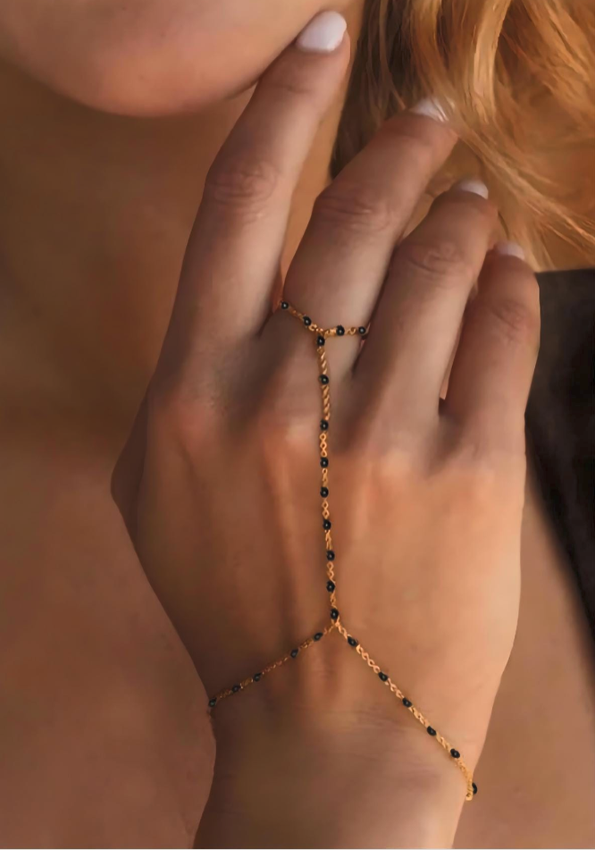 Hand wearing a delicate gold and black beaded bracelet against a blurred background